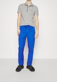 Gray polo shirt with a collar and black-and-red accents, paired with blue drawstring trousers and black sandals.