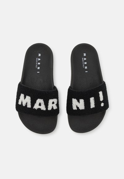Chanclas negras con una banda de tela suave que muestra "MAR! NI" en blanco. Parte superior texturizada y suela suave y flexible. Hechas en Italia.