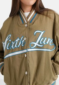 Olijfgroene bomberjack met blauw en wit borduurwerk "Sixth June," met knopen, gestreepte ribgebreide boorden en een gladde stoftextuur.
