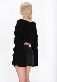 Maglione corto nero con texture a balze, dotato di maniche lunghe e una vestibilità ampia. Abbinato a pantaloni corti di jeans neri a vita alta.