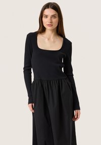 Svart långärmad topp med ribbad struktur och fyrkantig halsringning, kombinerad med en flödande svart kjol med elastisk midja.