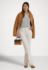 Kožená bunda v koňakovej farbe, pásikované polokošeľa, biele rozšírené nohavice, hnedé sandále, držiac malú tkanú kabelku s námorníckym klopou a zlatým logom.