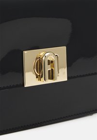 Borsa a tracolla in vernice nera con chiusura a gancio in tonalità oro. Superficie liscia, forma rettangolare elegante e cuciture dettagliate lungo i bordi.