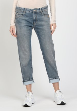 Hellblaue Jeans aus Denim mit lockerer Passform, aufgerollten Säumen, fünf Taschen und einer Zwei-Knopf-Verschluss. Kombiniert mit weißen Sneakers.