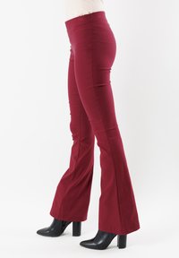 Pantaloni a zampa di elefante borgogna realizzati in un tessuto elasticizzato, con un alto punto vita, una texture liscia e cuciture a vista, abbinati a stivaletti neri con tacco.