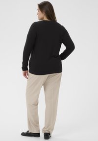 Un haut noir à manches longues associé à un pantalon beige clair. Le haut a un col rond et une coupe décontractée, tandis que le pantalon a une coupe droite.