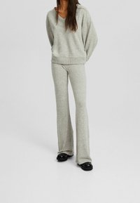 Set di abbigliamento loungewear grigio chiaro composto da un maglione oversize con scollatura a V e maniche a costine, abbinato a pantaloni svasati. Tessuto morbido con un delicato motivo a maglia.