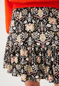 Zwarte, gerimpelde rok met bloemen- en vlinderpatronen in rood, geel en wit. Gemaakt van lichte stof en heeft een gelaagd ontwerp.
