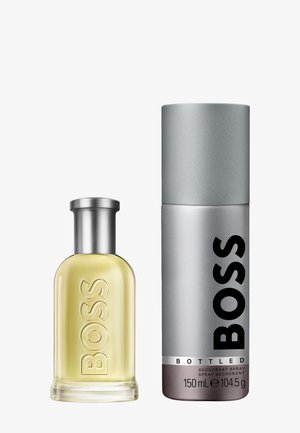 Bottiglia di vetro di colonia gialla con un tappo argentato accanto a un contenitore di deodorante argentato con testo nero, etichettato "BOSS Bottled."