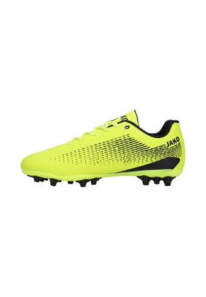 Felgele voetbalschoen met zwarte patronen, zwarte noppen en JAKO-logo op de hiel en tong, van opzij gezien.