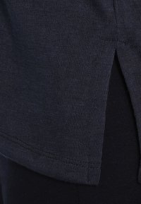 Dark navy shirt with a ribbed texture, featuring a side split hem. The fabric appears soft and lightweight, suitable for casual wear.