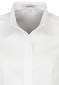 Vit skjorta med spetsig krage, tre synliga knappar, och etikett som visar märket "seidensticker" och storlek 36.