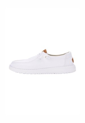 White canvas shoes with a round toe, featuring a light tan leather accent on the heel and a textured rubber sole.