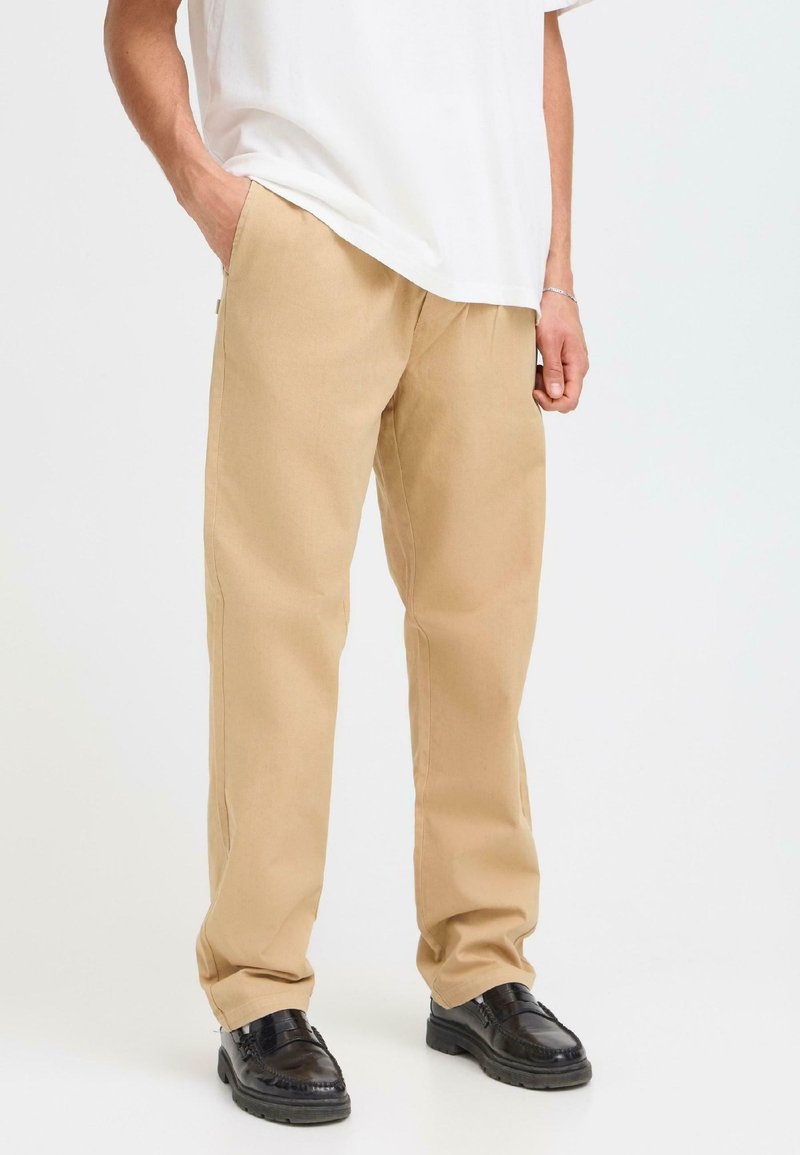 Beige wide-leg pants made of cotton, featuring side pockets and a smooth texture, paired with black shoes and a white loose-fitting shirt.