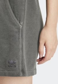 Gray cotton blend dress with a relaxed fit, ribbed texture, side pockets, and a dark logo at the hem. Close-up of a hand resting on the fabric.