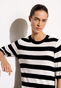 Striped knit sweater in black and white, short sleeves, crew neck, smooth texture, displayed with a model against a plain background.