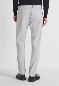 Lichtgrijze, gemêleerde broek met een relaxte pasvorm, voorzien van een stretchy tailleband en twee achterzakken, gecombineerd met zwarte schoenen.