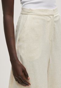Lichtbeige linnenbroek met een gladde textuur, gestructureerd ontwerp en zijzakken. Opvallende hoge taille en schone, minimale stikseldetails.