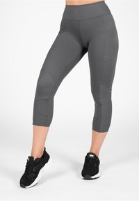 Grijze cropped leggings gemaakt van een gladde, rekbare stof met een aansluitende pasvorm en contrasterende accentstiksels, gecombineerd met zwarte sneakers.