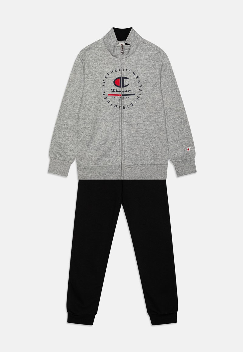 Chaqueta gris con cremallera y logo en el pecho, pantalones deportivos negros a juego. Ambas prendas están hechas de una tela suave y cuentan con puños y cintura de canalé.