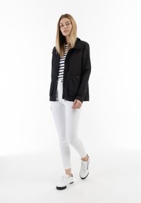 Giacca leggera nera con chiusura a zip, vita stretta e due tasche frontali, abbinata a jeans skinny bianchi e sneakers bianche.