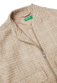 Beżowa kurtka o fakturowanej powierzchni, z przodem na suwak, kołnierzem i widocznymi przeszyciami. Podszewka z wewnętrzną metką marki.