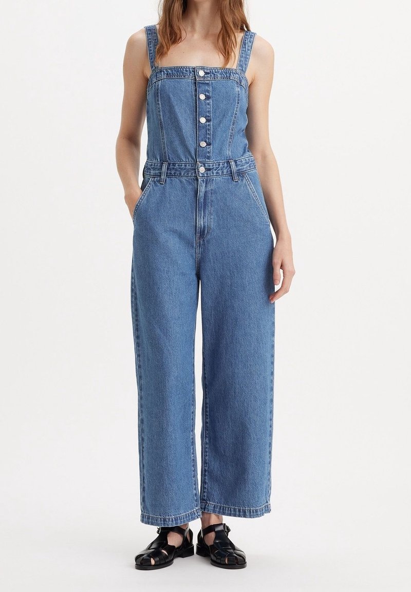 Denim overall i ljusblått, med vida ben, fyrkantig halsringning, framknappar och justerbara remmar. Slät textur med fickor.