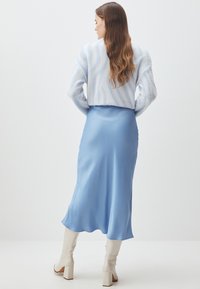 Abito in satin blu chiaro con una silhouette fluida, abbinato a un maglione corto in peluche con motivo a onde e stivali bianchi fino al ginocchio.