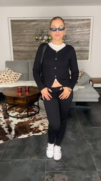Black cardigan with buttons over a white top, paired with black pants and white sneakers. Accessories include black sunglasses and a handbag.