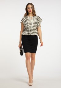 Peplum-bluse i høj-kontrast sort og hvidt mønster med flæser på ærmerne, parret med en tætsiddende sort nederdel og nude stilethæle, mens hun holder en sort clutch.