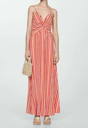 Femme portant une robe longue rayée sans manches avec un col en V dans des tons orange, rose et rouge, tenant un petit sac tressé et portant des sandales beiges.