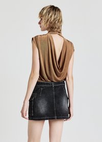 Top in bronzo drappeggiato con schiena a V, abbinato a una mini gonna in denim nera con tasche laterali e una texture sbiadita.