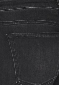 Svarta denimjeans med en mjuk textur, med en bakficka och kontrasterande sömmar längs sömmarna. Minimalistisk design.