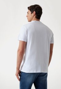 Witte katoenen T-shirt met korte mouwen en een ronde hals, met een gladde textuur en een ontspannen pasvorm, gecombineerd met een blauwe denim jeans.