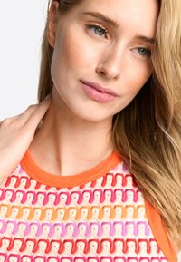 Multikleurige gebreide top met oranje rand, complexe luskoffers in roze, rood en geel op een crème achtergrond. Zachte textuur.