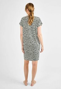 Abito con stampa leopardata a maniche corte, realizzato in tessuto leggero. Sfondo prevalentemente chiaro con macchie nere, design che arriva fino al ginocchio.