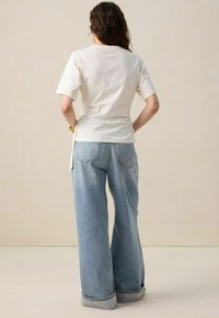 T-shirt blanc à manches courtes avec un ourlet arrondi, associé à un jean large bleu clair avec de grandes poches arrière et des poignets retroussés.