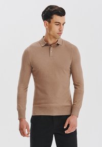 Brązowy sweter polo z długim rękawem i kołnierzykiem, o miękkiej fakturze i z trzema guzikami, w połączeniu z ciemnymi spodniami.