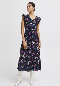 Blommig maxi-klänning i svart, med rosa, blå och vita blommor. Har en V-ringning, volangärmar och en lager-på-lager, flödande kjol. Bärs med vita stövlar.