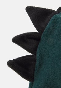 Grønn strikket stoff med svarte fleece-spisse langs kanten, med en teksturert overflate og en myk, avrundet finish.