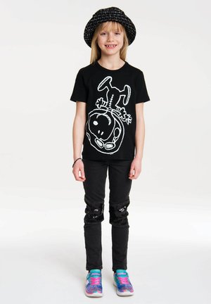 Black t-shirt featuring a white graphic design, paired with black jeans that have sequined knee accents and colorful sneakers.