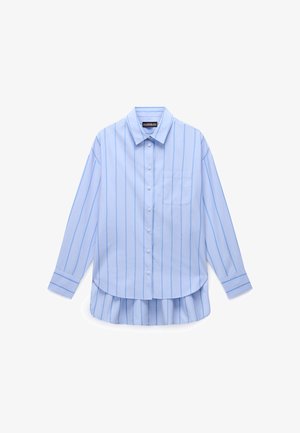 Svetlo modra majica z dolgimi rokavi in navpičnimi belimi črtami, zapenjanje na gumbe in žepom na prsih; ima zaobljen rob in naborke na hrbtni strani.