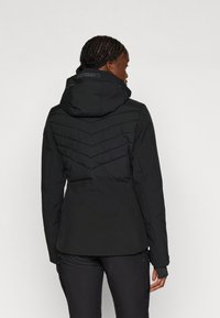 Veste noire isolée avec capuche, présentant un motif matelassé en chevron au dos, une texture lisse et des poignets ajustables.