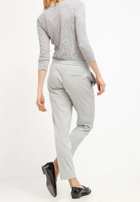 Ljust grå tapered byxor med en slät yta och elastisk midja. Har en enkel bakficka och bärs med svarta skor.