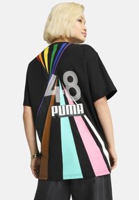 T-shirt nera in cotone con audaci strisce diagonali multicolori, il numero "48" e "PUMA" stampato in grande testo bianco sul retro.