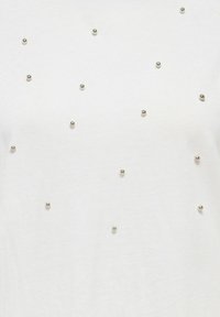 Biały materiał z równomiernie rozmieszczonymi małymi metalicznymi srebrnymi koralikami przyczepionymi w rozproszonym wzorze na powierzchni.