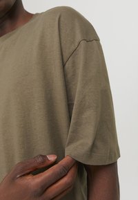 Olivengrøn kortærmet t-shirt lavet af blødt bomuld. Har rund halsudskæring og afslappet pasform med synlige sting på ærmekanterne.