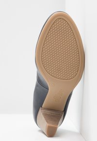 Chaussure en cuir noir avec une semelle en caoutchouc texturée, dotée d'un talon bas empilé et de détails de couture subtils le long de la tige. Étiquette taille 37 visible.