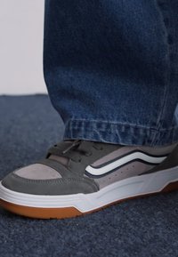 Sapatilha de camurça cinza e têxtil com riscas brancas, sola de borracha e colarinho almofadado, combinada com jeans azul escuro.