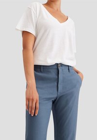 Vit, löst sittande kortärmad T-shirt med V-hals som kombineras med blå, skräddarsydda byxor med knappstängning och sidofickor.